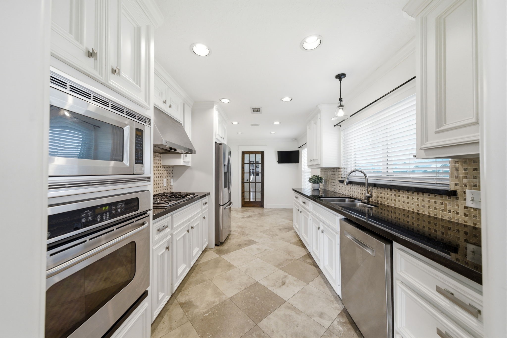 6427 Waltway Drive Houston, TX 77008 - Photo 8 of 37 Bright, modern kitchen with stainless steel appliances, white cabinetry, and granite countertops. Features a basketweave tiled backsplash, recessed lighting, and a large window for natural light.