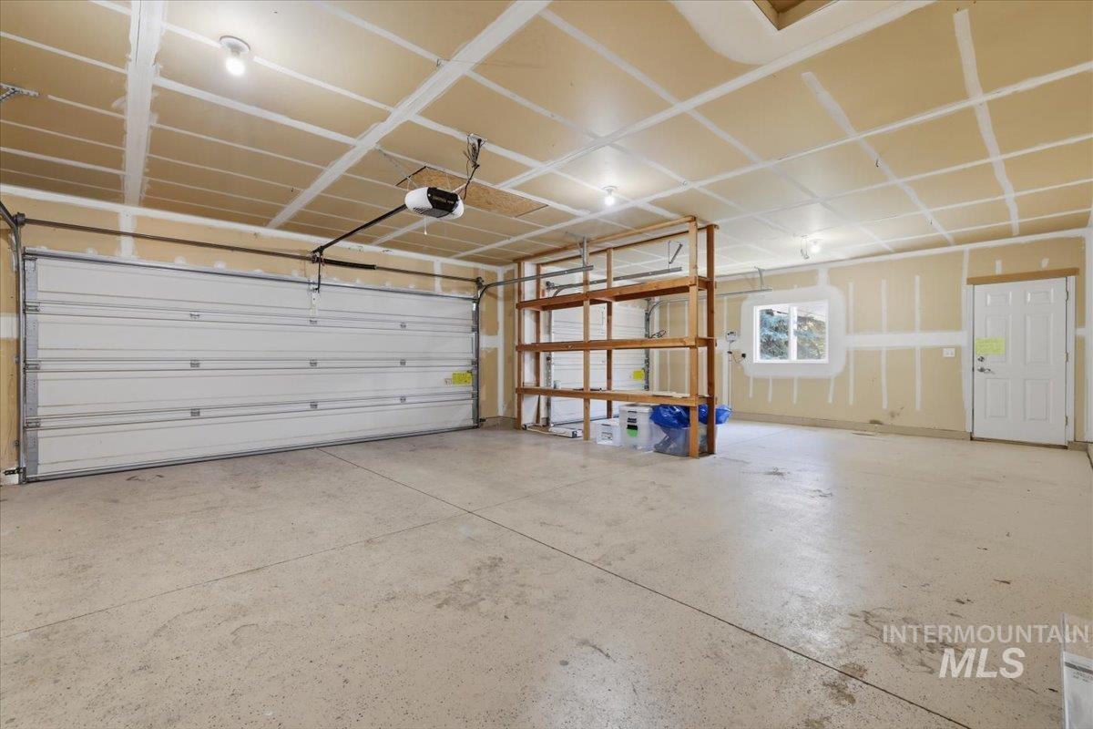 2075 North Springland Place Boise, ID 83713 - Photo 48 of 49 Spacious garage featuring a concrete floor, overhead lighting, an automatic garage door opener, built-in wooden shelving, and a side access door