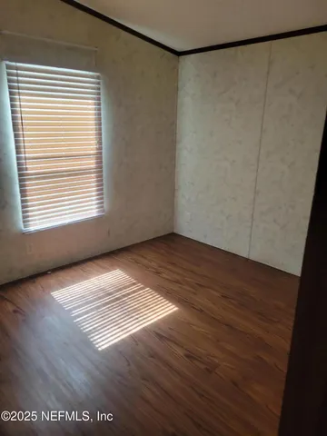 a view of an empty room with a window and wooden floor