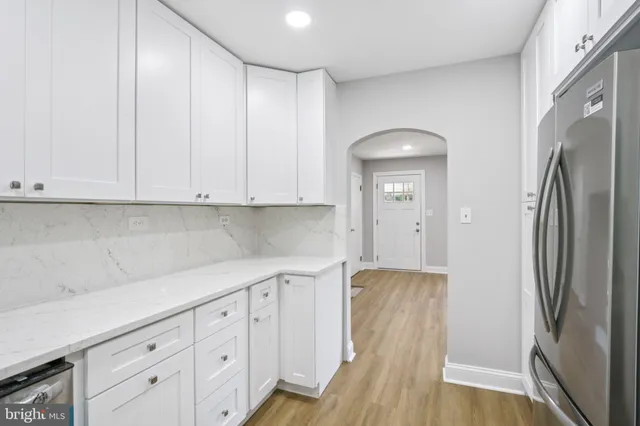 a kitchen with stainless steel appliances granite countertop a refrigerator a sink and white cabinets with wooden floor