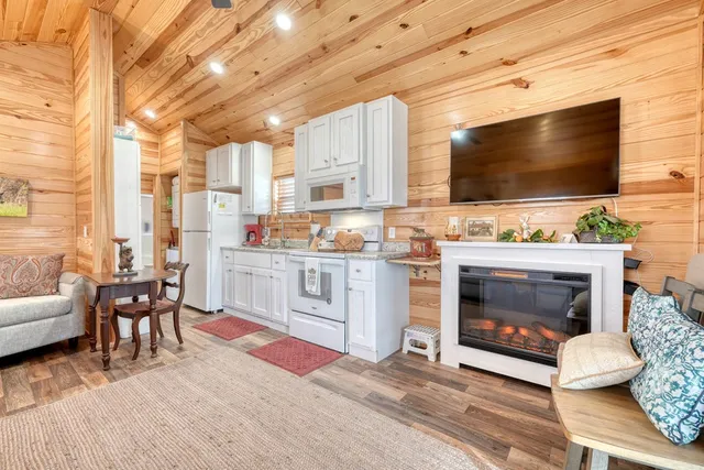 a living room with stainless steel appliances furniture a fireplace a flat screen tv and kitchen view
