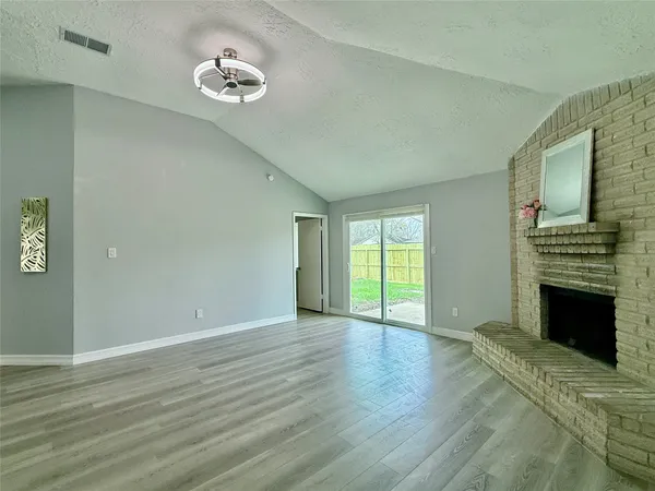 a view of an empty room with wooden floor fireplace and a window