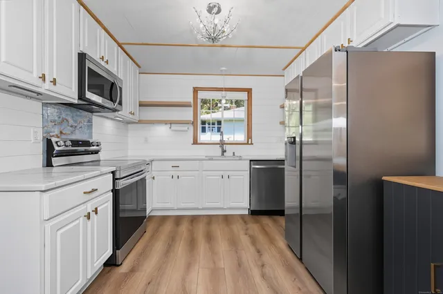 a kitchen with stainless steel appliances a white stove top oven a sink dishwasher and a refrigerator with wooden floor