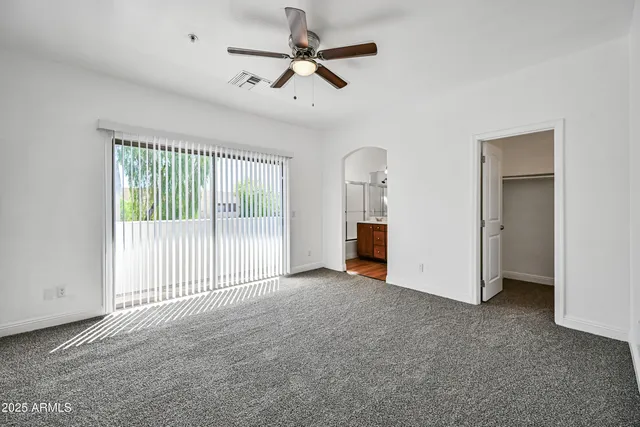 an empty room with chandelier fan and windows
