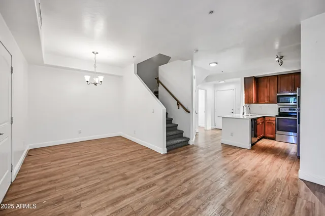 a view of empty room with wooden floor and kitchen