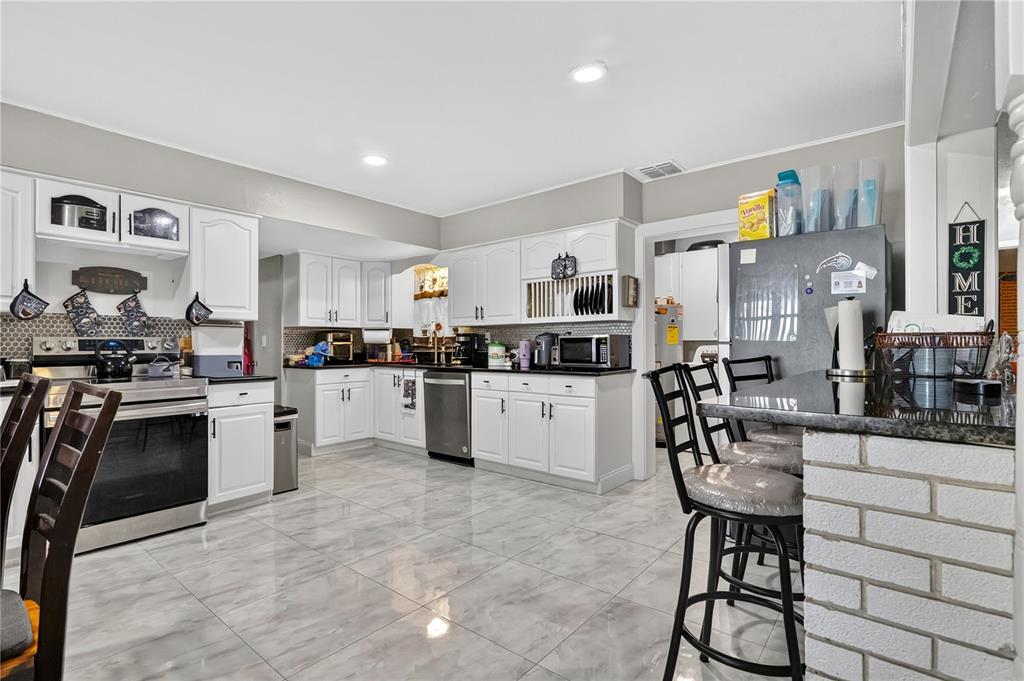 9727 Bear Lake Road Apopka, FL 32703 - Photo 9 of 22 a kitchen with stainless steel appliances a refrigerator a stove top oven a sink a dining table and chairs