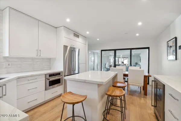 a kitchen with stainless steel appliances kitchen island granite countertop a refrigerator a stove and white cabinets with wooden floor