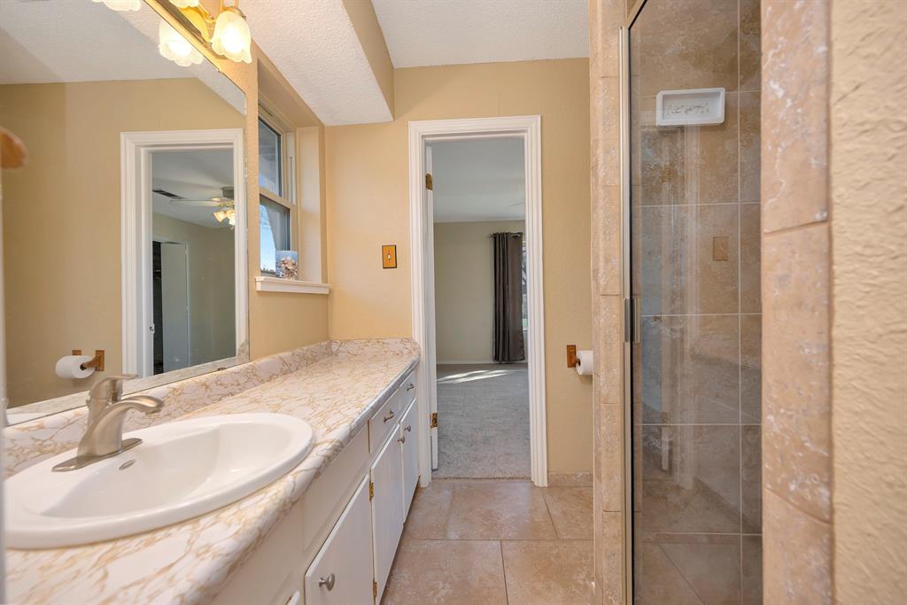 1761 Cynthia Lane Hurst, TX 76054 - Photo 32 of 40 a bathroom with a granite countertop sink a mirror and a shower