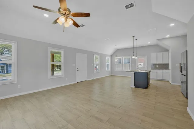 an empty room with chandelier fan and windows