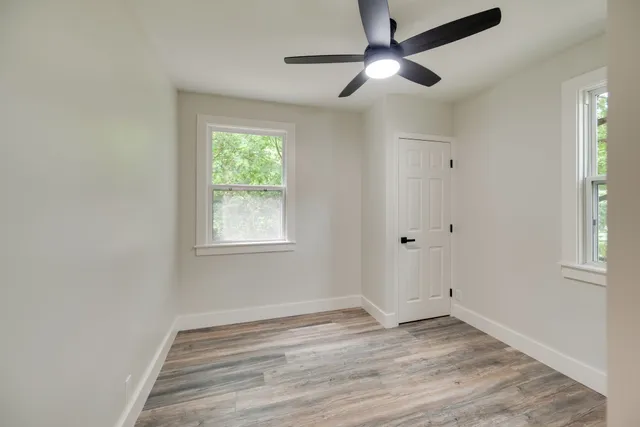 a view of empty room with wooden floor and fan