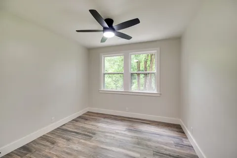 an empty room with wooden floor ceiling fan and windows