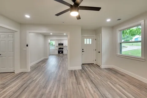 a view of a big room with wooden floor a ceiling fan and windows
