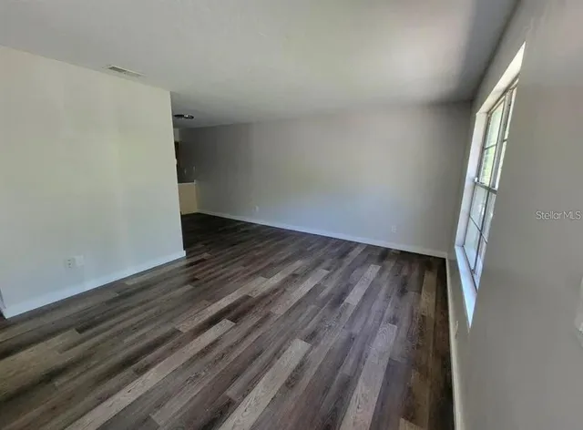 a view of an empty room with wooden floor and a window