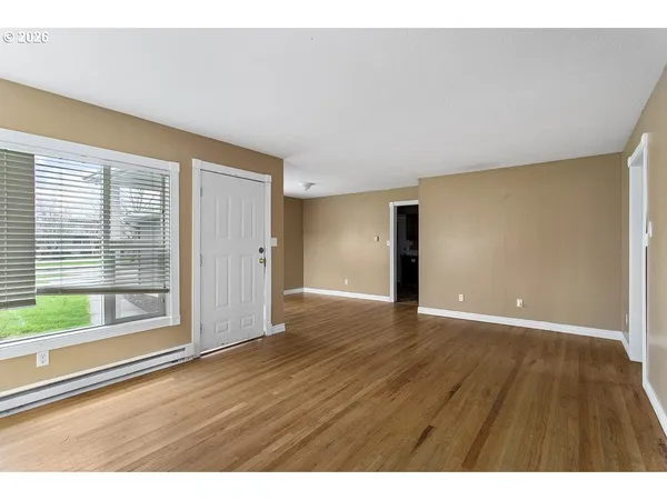 a view of an empty room with wooden floor and a window