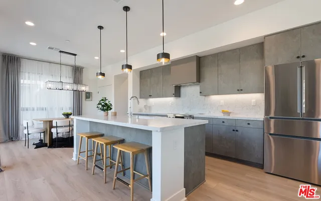 a kitchen with stainless steel appliances granite countertop a refrigerator a sink dishwasher a stove and a dining table with wooden floor