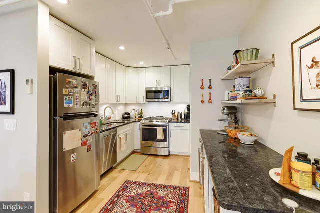 a kitchen with stainless steel appliances granite countertop a refrigerator oven a sink dishwasher and white cabinets with wooden floor