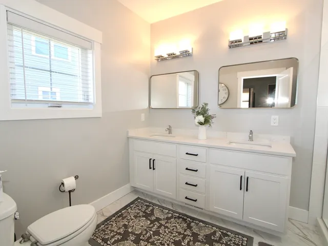 a bathroom with a toilet a sink a mirror a window and vanity