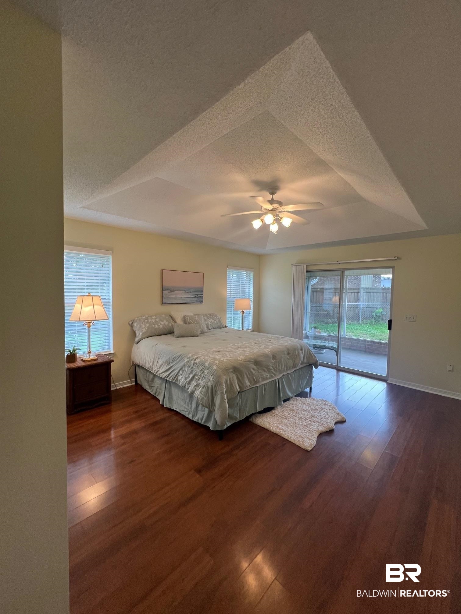 2204 Club House Drive Lillian, AL 36549 - Photo 10 of 38 Bedroom featuring access to outside, a textured ceiling, wood finished floors, multiple windows, and a tray ceiling