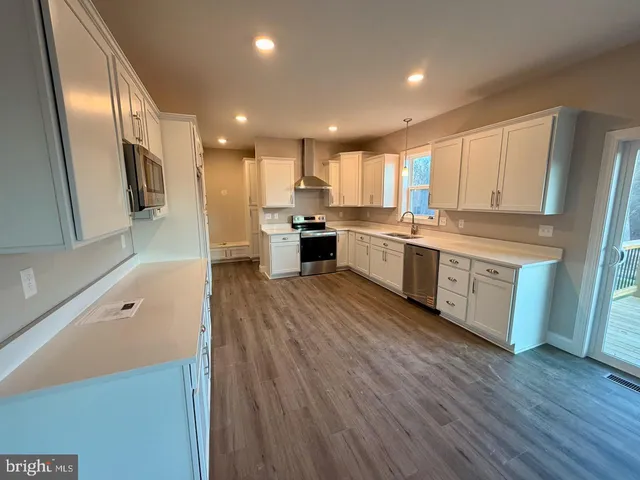 a large kitchen with stainless steel appliances a large counter top and wooden floors