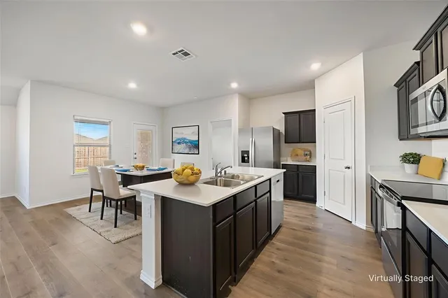 a kitchen with stainless steel appliances a sink a stove a refrigerator cabinets and a dining table