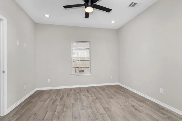 an empty room with wooden floor fan and windows