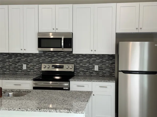 a kitchen with stainless steel appliances granite countertop a stove a refrigerator and a white cabinets