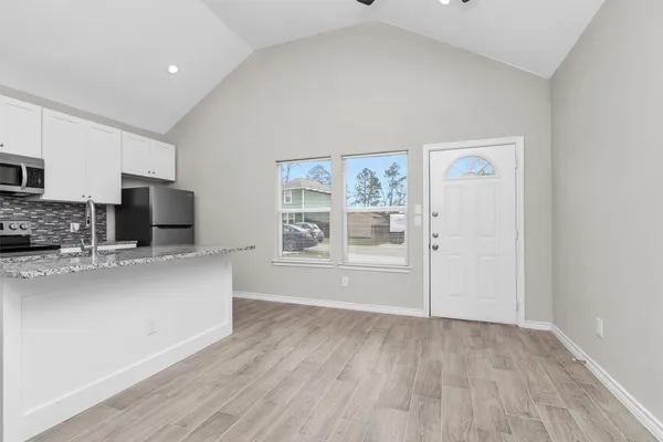 a living room with stainless steel appliances wooden floor and a view of kitchen