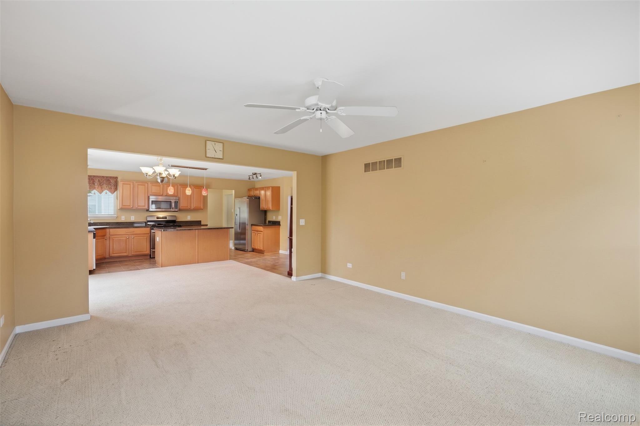 170 Fairhill Way Howell, MI 48843 - Photo 15 of 46 Carpeted living area with a ceiling fan, featuring an open archway to a kitchen with wood-finish cabinetry, dark countertops, and stainless steel appliances