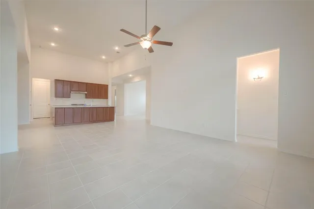 an empty room with chandelier fan and kitchen view