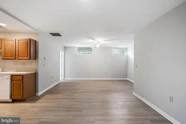 a view of an empty room with wooden floor and a kitchen