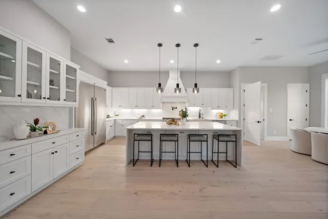 a kitchen with stainless steel appliances granite countertop a stove a sink dishwasher a refrigerator and white cabinets with wooden floor