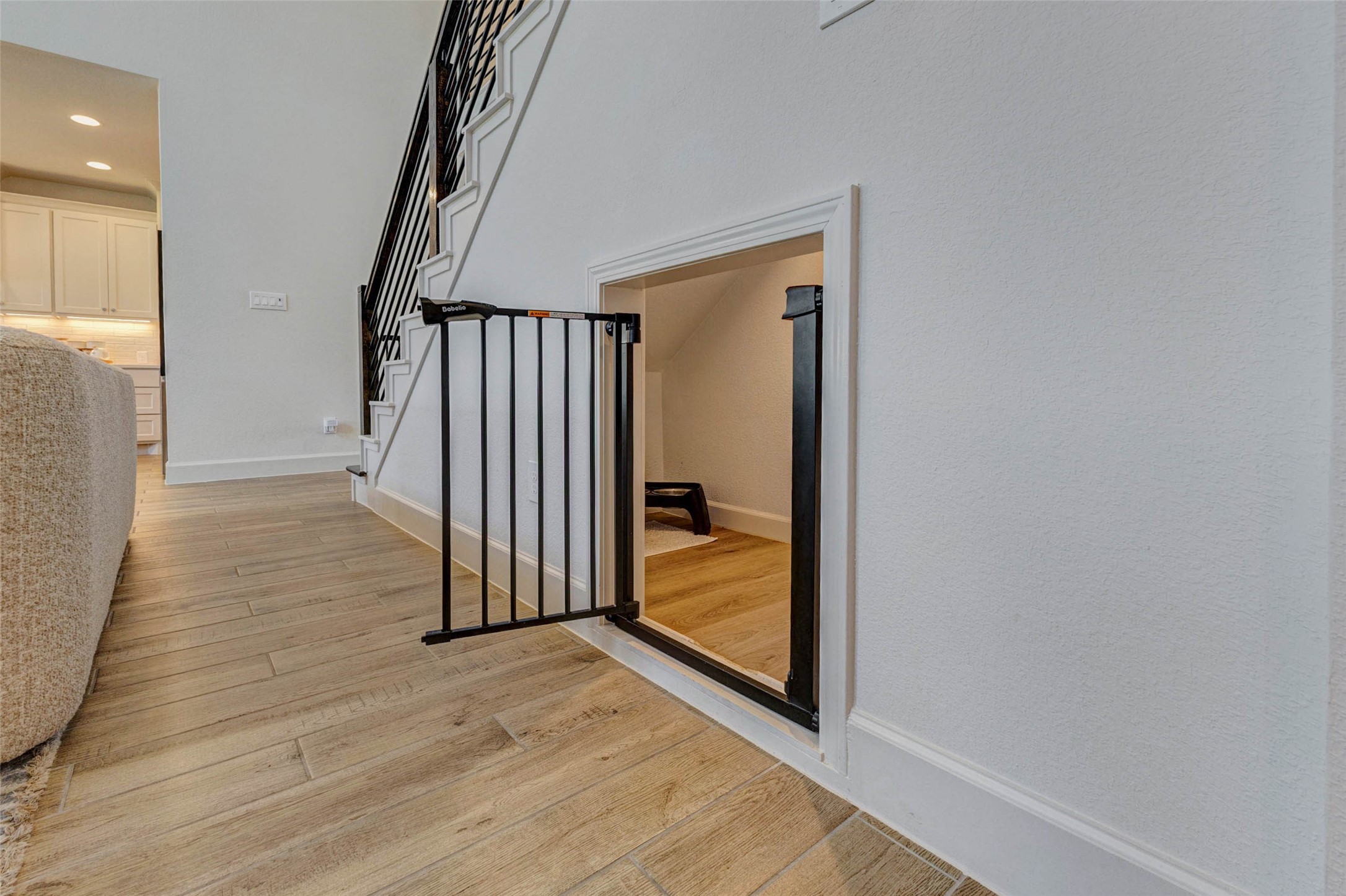 4322 Southpoint Way Fulshear, TX 77441 - Photo 23 of 50 Cozy nook under a staircase, featuring a small door with a safety gate. Ideal for storage or a pet area, it adds functional use to the space. The area is adjacent to an open kitchen with modern features and hardwood flooring.