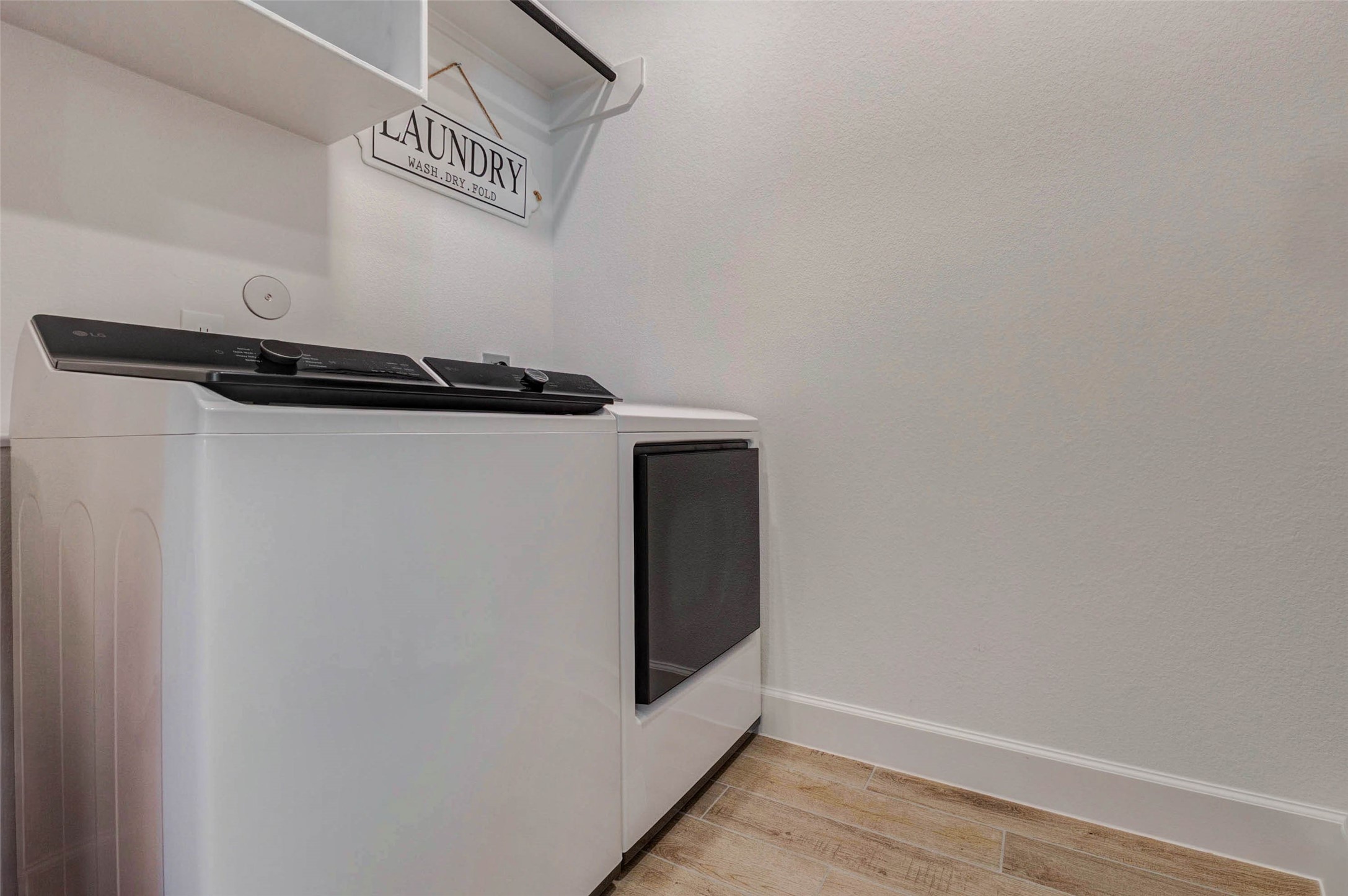 4322 Southpoint Way Fulshear, TX 77441 - Photo 25 of 50 Laundry room with a washer and dryer. The space features white walls, light wood flooring, and a shelf above the appliances for storage.