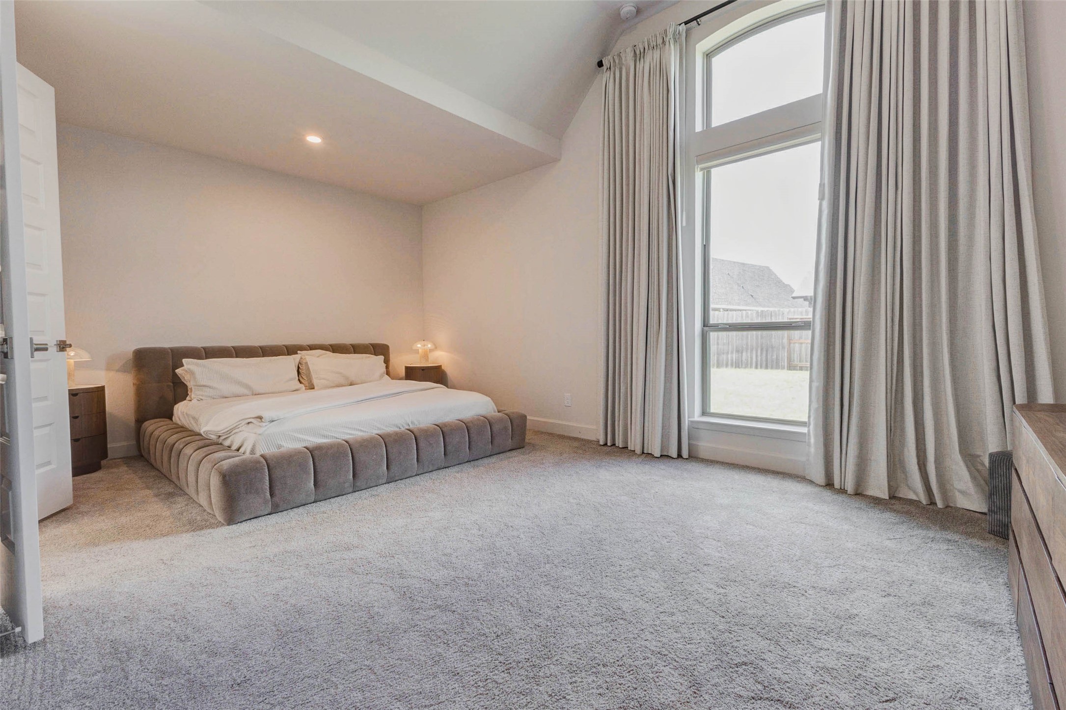 4322 Southpoint Way Fulshear, TX 77441 - Photo 28 of 50 Primary bedroom features high ceilings, and a large window with elegant curtains, offering ample natural light and a serene view. The neutral color scheme and soft carpeting add to the room's cozy and inviting atmosphere.