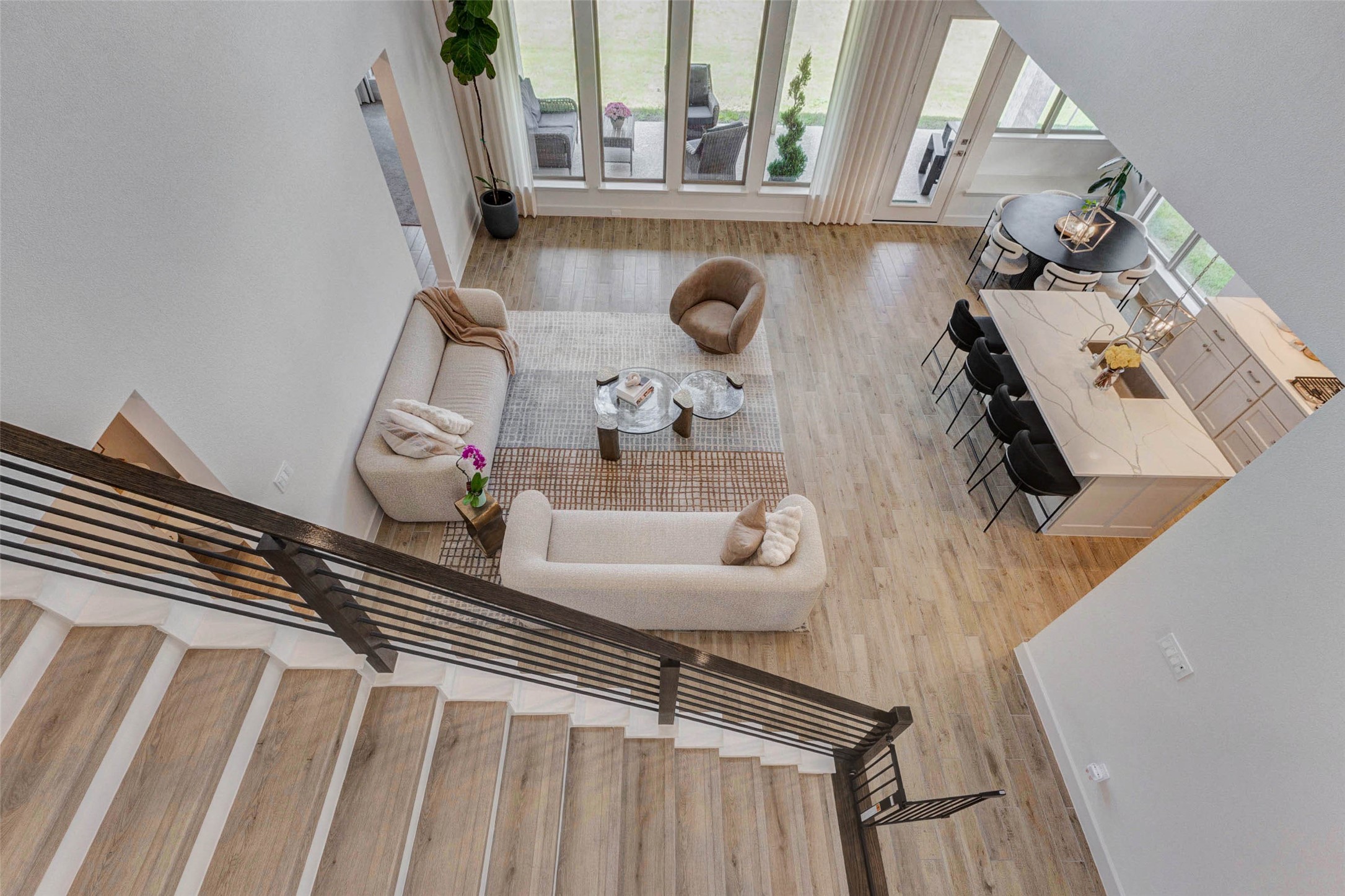 4322 Southpoint Way Fulshear, TX 77441 - Photo 2 of 50 Modern, open-concept living area with hardwood looking floors, a cozy seating arrangement, and a stylish kitchen island with bar seating. Large windows offer plenty of natural light, enhancing the spacious feel. The view from the staircase highlights the inviting layout, ideal for entertaining and family gatherings.