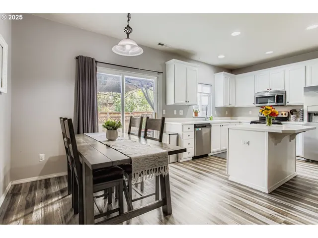 a open dining room with stainless steel appliances kitchen island granite countertop a stove a sink a refrigerator and white cabinets with wooden floor