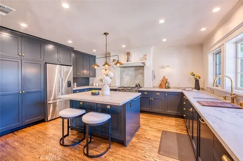 a kitchen with stainless steel appliances granite countertop a sink a stove a refrigerator and island with wooden floor