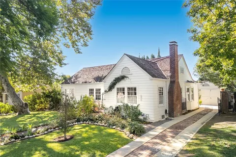 a view of a white house next to a yard with plants and trees