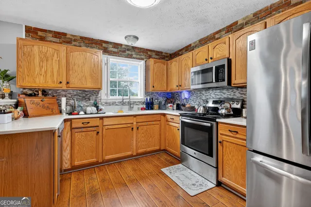 a kitchen with stainless steel appliances granite countertop a refrigerator a sink dishwasher a stove with wooden cabinets and floor