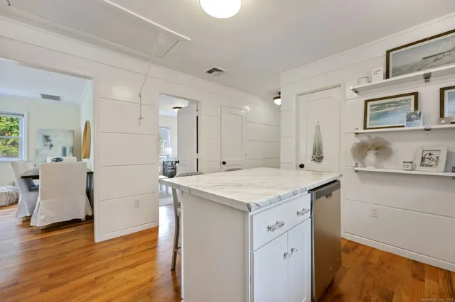 a hall with kitchen island white cabinets and wooden floor