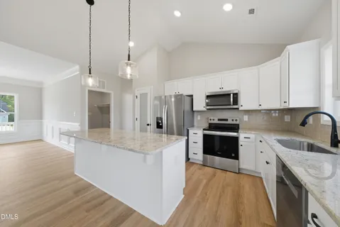 a large kitchen with stainless steel appliances granite countertop a stove a sink dishwasher a refrigerator white cabinets and wooden floor next to a window