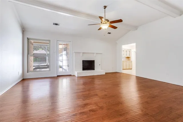 an empty room with wooden floor chandelier fan and windows