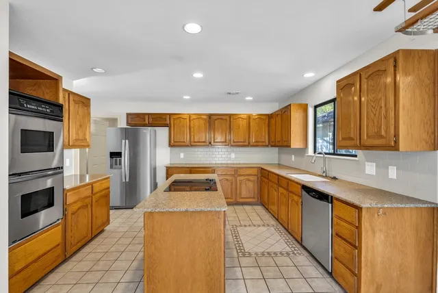 a kitchen with stainless steel appliances granite countertop a sink a stove top oven a refrigerator cabinets and living room view