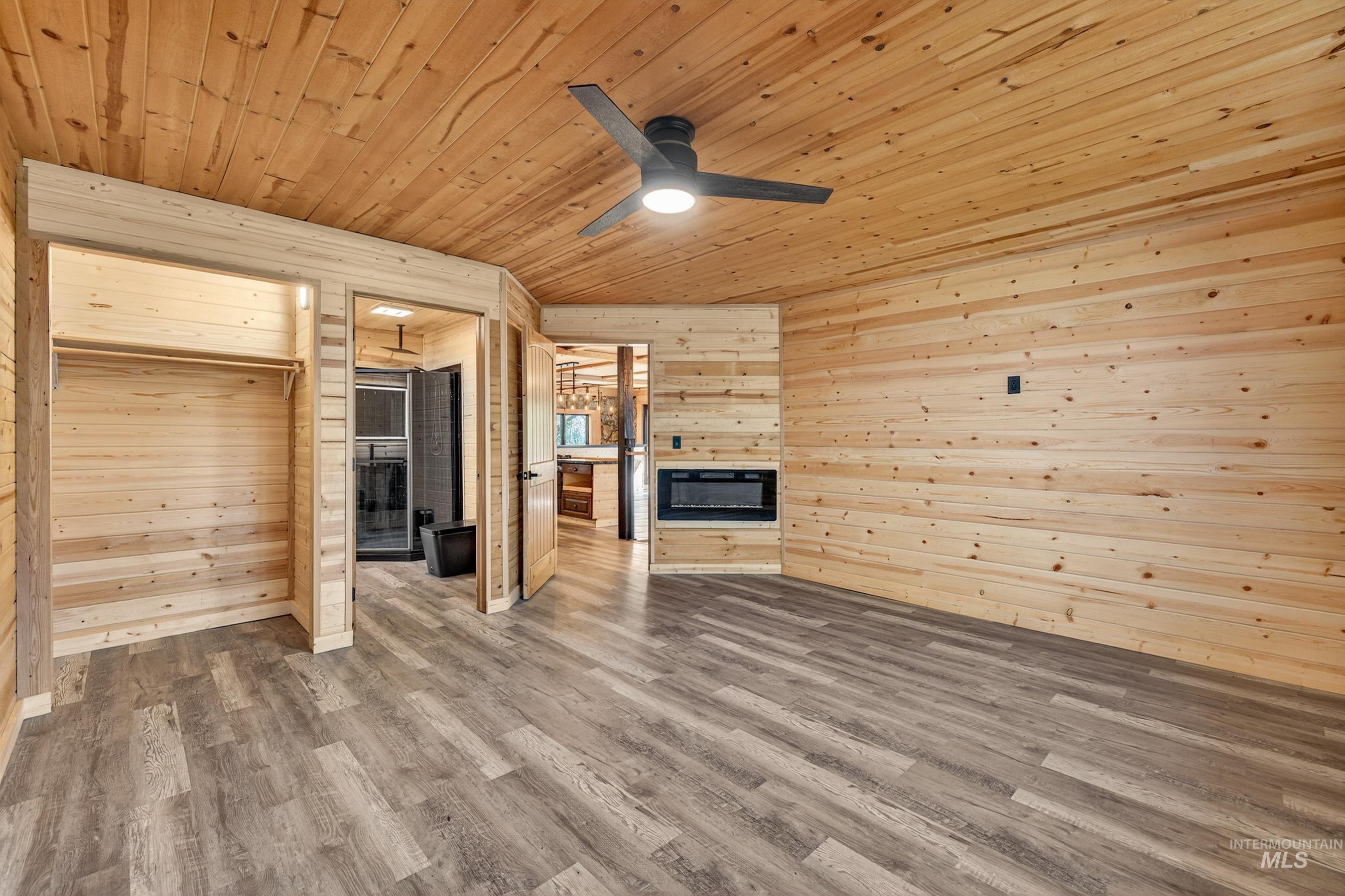 543 North Main Street Riggins, ID 83549 - Photo 22 of 46 Unfurnished living room featuring a glass covered fireplace, a ceiling fan, wooden ceiling, dark wood-style floors, and wooden walls