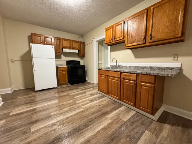 a kitchen with stainless steel appliances granite countertop a refrigerator a sink dishwasher a stove with wooden cabinets and floor