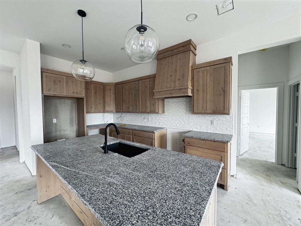 1012 Katie Court Azle, TX 76020 - Photo 5 of 7 Kitchen featuring decorative light fixtures, tasteful backsplash, unfinished concrete floors, a kitchen island with sink, and wood finish cabinets