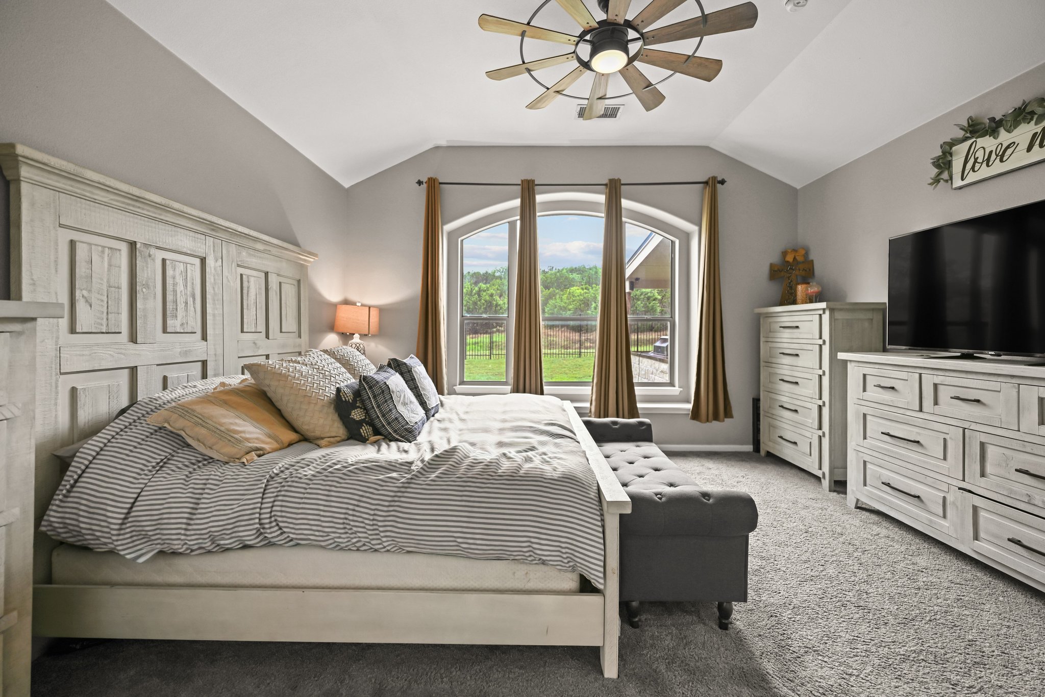 5528 Wild Foxglove Road Spicewood, TX 78669 - Photo 12 of 38 Arched windows with outdoor views, vaulted ceiling, ceiling fan with light fixture, gray wall paint, and gray carpet flooring