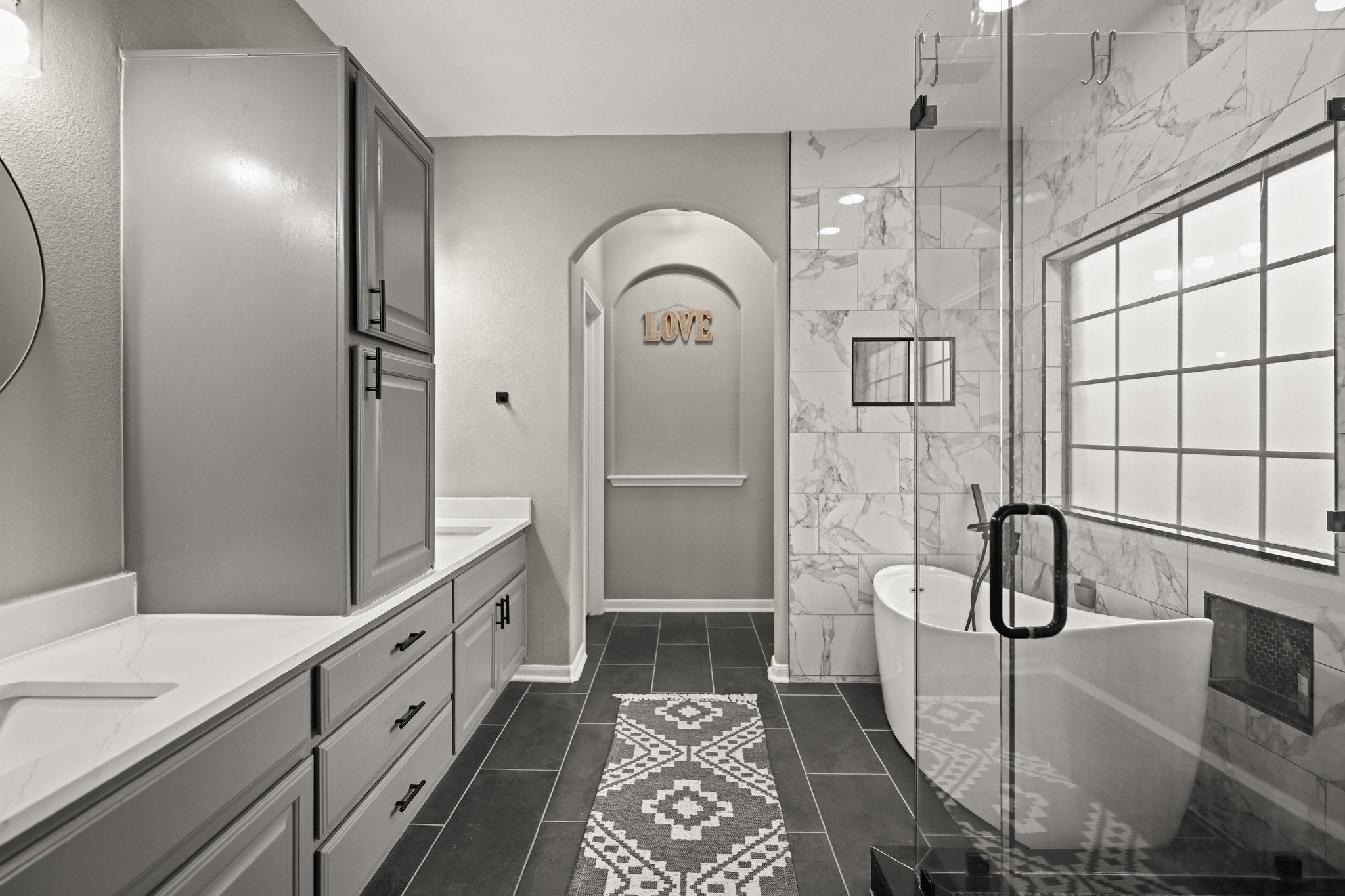 5528 Wild Foxglove Road Spicewood, TX 78669 - Photo 17 of 38 Spacious bathroom featuring a frameless glass shower enclosure, a freestanding soaking tub, dual vanities with quartz countertops, gray cabinetry, and dark tile flooring