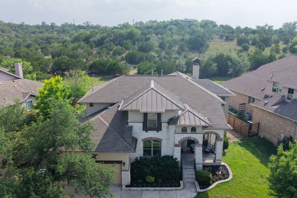 5528 Wild Foxglove Road Spicewood, TX 78669 - Photo 2 of 38 Stone and stucco facade featuring a covered front porch with arched entries, a multi-gabled roofline with metal accents, and a two-car garage