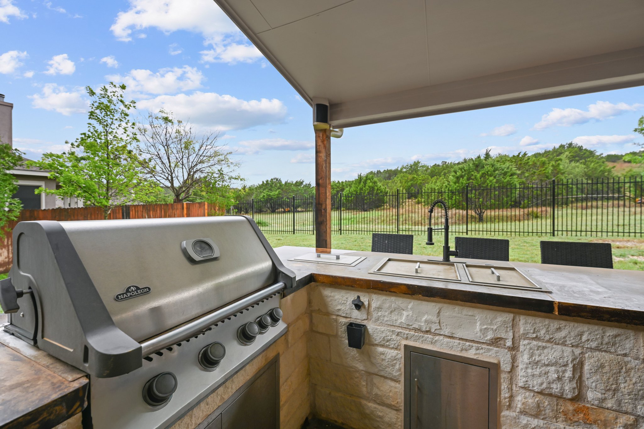 5528 Wild Foxglove Road Spicewood, TX 78669 - Photo 34 of 38 Covered outdoor kitchen featuring a built-in stainless steel grill, stone veneer base, integrated sink with a matte black faucet, and bar seating